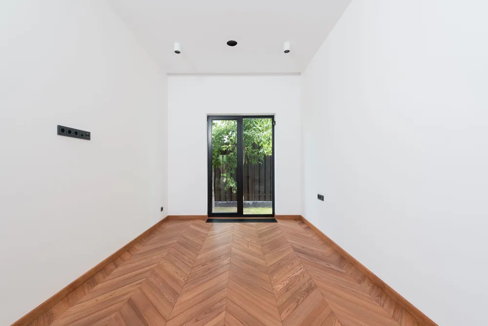 A newly laid herringbone parquet in a bright room with a garden door